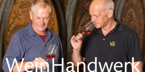 Zwei Männer begutachten den RoterBur-Roséwein vor großen hölzernen Weinfässern.
