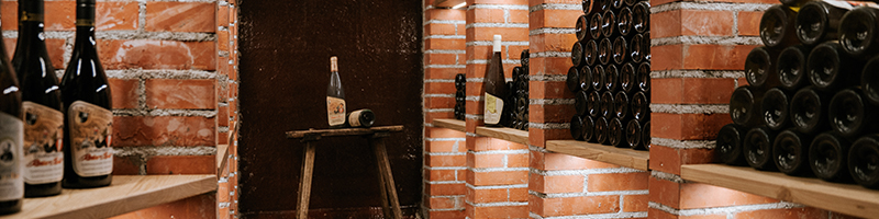Weinflaschen auf gemauerten Regalen in einem Keller mit einem Holzschemel in der Mitte.