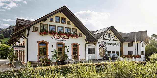 Weißes Gebäude mit Blumenkästen und einer Wandmalerei an der Seite, umgeben von Grünflächen. Weißes Gebäude mit Blumenkästen und einer Wandmalerei an der Seite, umgeben von Grünflächen.