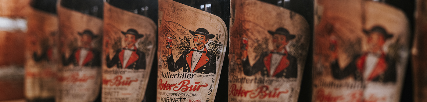 Reihe von Weinflaschen mit Vintage-Etiketten, auf denen ein Mann im Anzug Weingläser hält.