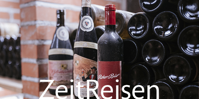 Horizontal in Regalen gelagerte Weinflaschen mit dem Schriftzug ZeitReisen darüber.